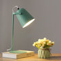 Groene versie van de bureaulamp met brandende kap, op een boek naast een vaasje met roosjes. 9
