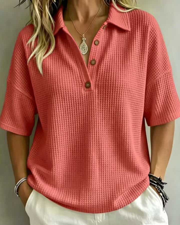 Voorkant van het koraalrode wafelpoloshirt met knoopsluiting, gedragen door een model met witte broek 4