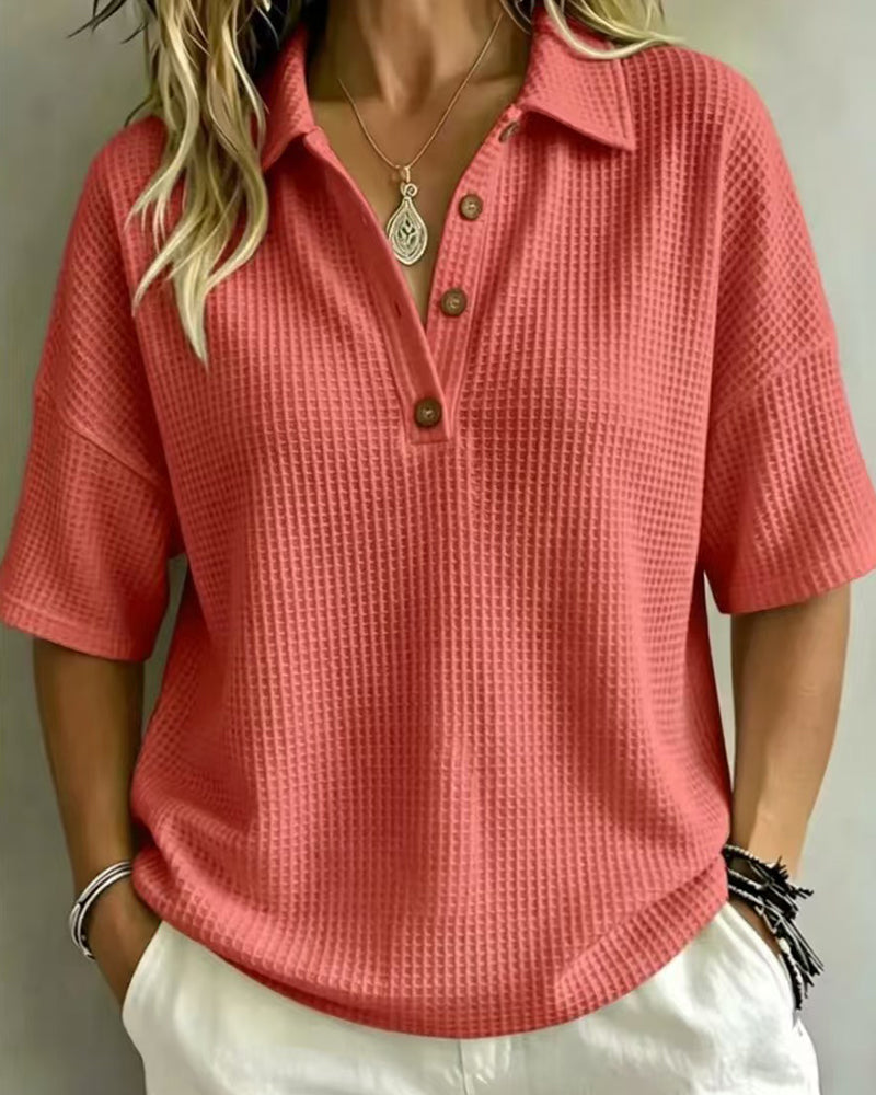 Voorkant van het koraalrode wafelpoloshirt met knoopsluiting, gedragen door een model met witte broek 4