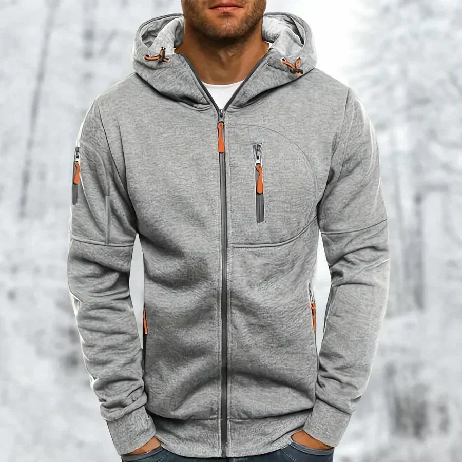 Man draagt de lichtgrijze gemêleerde hoodie met oranje ritstrekkers, geborduurde structuur zichtbaar, voor een besneeuwde achtergrond. 8