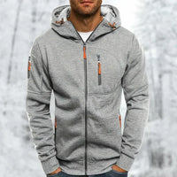 Man draagt de lichtgrijze gemêleerde hoodie met oranje ritstrekkers, geborduurde structuur zichtbaar, voor een besneeuwde achtergrond. 8