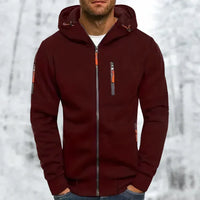 Man draagt de bordeauxrode hoodie met oranje ritstrekkers en grijze rits, handen in de zakken, met winters bos op de achtergrond. 4