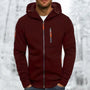 Man draagt de bordeauxrode hoodie met oranje ritstrekkers en grijze rits, handen in de zakken, met winters bos op de achtergrond. 4