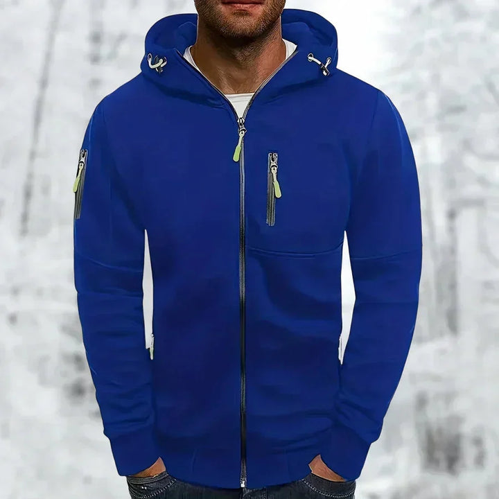 Man draagt de koningsblauwe hoodie met limoengroene ritstrekkers, dichtgeritst voorzijde met borstzakje, voor een besneeuwde achtergrond. 1