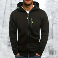 Zwarte hoodie met limoengroene ritstrekkers en capuchon, gedragen door een man met handen in de zakken voor een winterse achtergrond. 7
