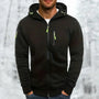 Zwarte hoodie met limoengroene ritstrekkers en capuchon, gedragen door een man met handen in de zakken voor een winterse achtergrond. 7