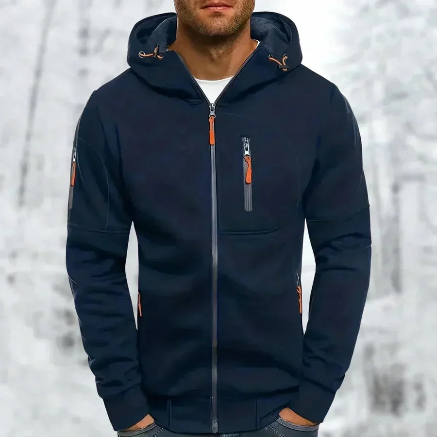 Donkerblauwe hoodie met oranje ritstrekkers en ribboord, gedragen door een man met handen in de broekzakken voor een besneeuwde achtergrond. 5