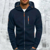 Donkerblauwe hoodie met oranje ritstrekkers en ribboord, gedragen door een man met handen in de broekzakken voor een besneeuwde achtergrond. 5