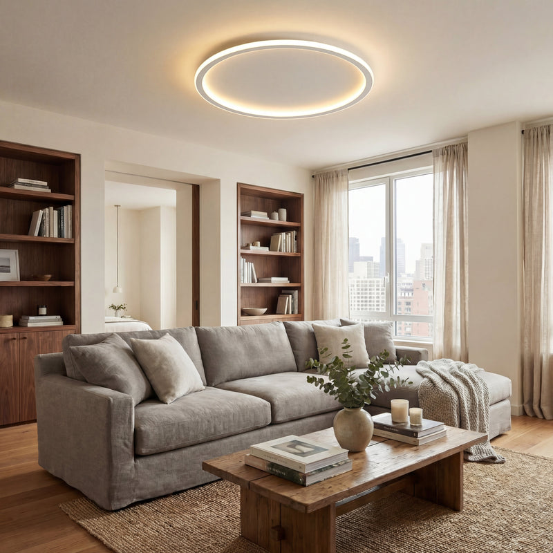 Ronde lichtring aan het plafond van een woonkamer met grijze hoekbank, houten salontafel, boekenkasten en een raam met gordijnen. 5
