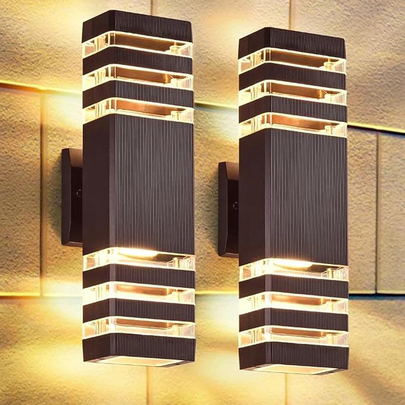 Twee donkerbruine, rechthoekige wandlampen met ribbels en doorzichtige stroken stralen warm licht omhoog en omlaag over een stenen muur. 1