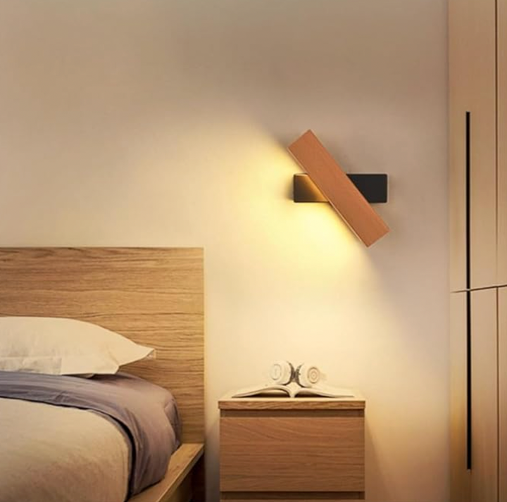 Schuin gedraaide houten wandlamp met zwarte steun boven een nachtkastje met boek en koptelefoon naast een houten bed. 6