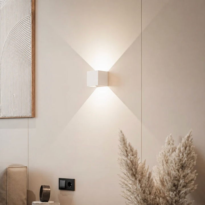 Witte kubuslamp op een beige muur met schilderij, pampasgras en stopcontact, het licht verspreidt zich omhoog en omlaag. 12