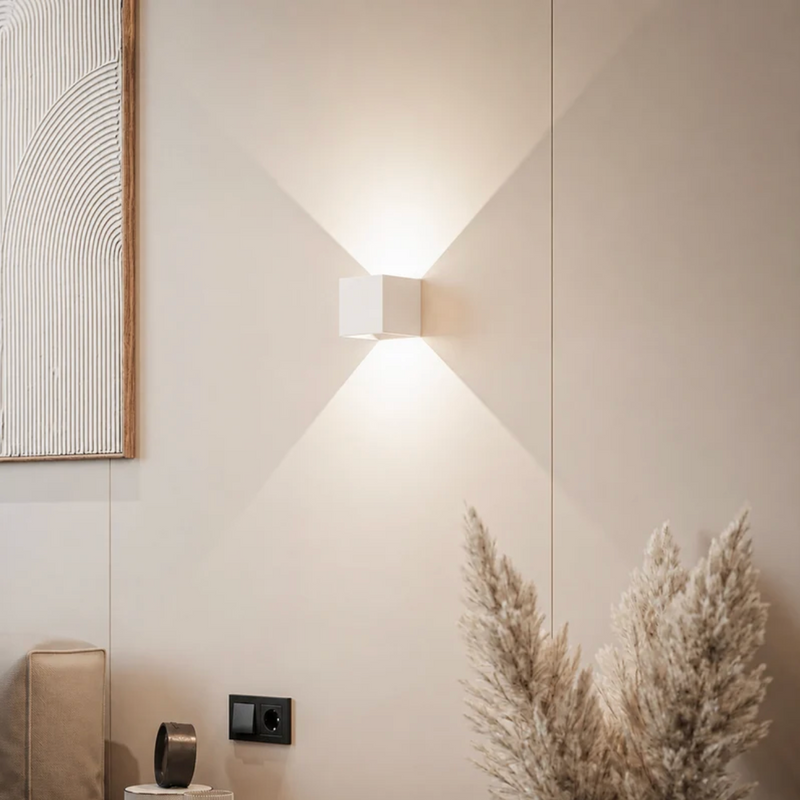 Witte kubuslamp op een beige muur met schilderij, pampasgras en stopcontact, het licht verspreidt zich omhoog en omlaag. 12