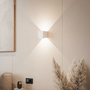 Witte kubuslamp op een beige muur met schilderij, pampasgras en stopcontact, het licht verspreidt zich omhoog en omlaag. 12