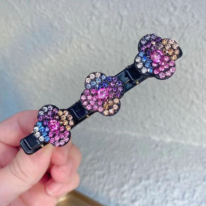 Haarspeld met drie veelkleurige strassbloemen in roze, blauw, paars en oranje, op een zwarte klem, vastgehouden in een hand. 5