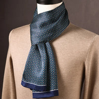 Blauwe sjaal met klein blokjespatroon in wit en turquoise en een marineblauwe rand, om een pop met beige trui. 24