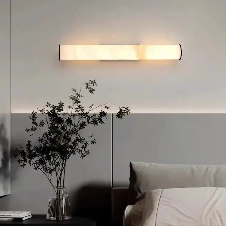 Marmeren wandlamp horizontaal gemonteerd boven een bed op een tweekleurige muur, naast een glazen vaas met bladtakken. 16