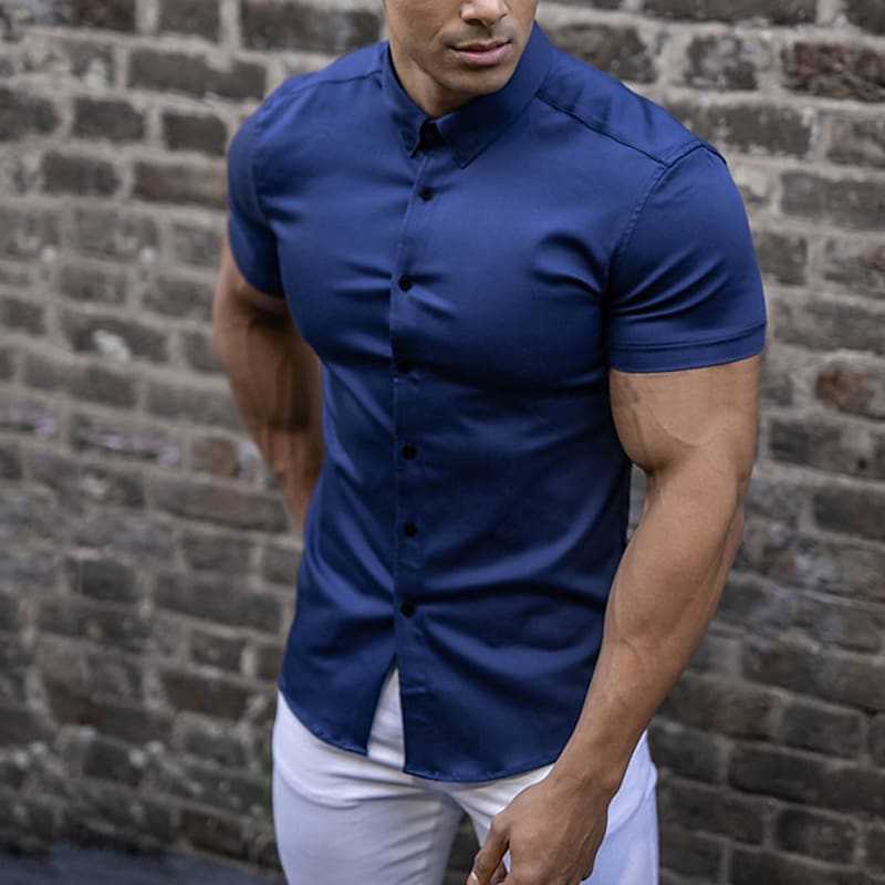 Blauw overhemd met korte mouwen, gedragen door een man in een witte broek voor een bakstenen muur. 3