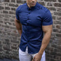 Blauw overhemd met korte mouwen, gedragen door een man in een witte broek voor een bakstenen muur. 3