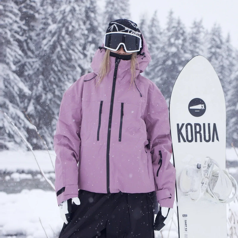 Model in roze-paarse ski-jack met zwarte ritsen staat naast een witte snowboard in vallende sneeuw. 3