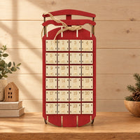 Rode houten sleekalender met 24 vakjes en jutetouw, staand op een houten plank met kerstdecoratie en een houten huisje ernaast. 1