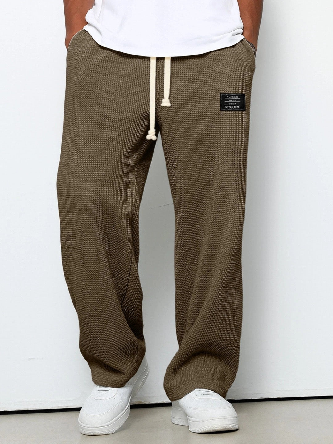 Voorkant van de wafelgebreide broek in bruingroen, gedragen door een model met wit shirt en witte sneakers. 5