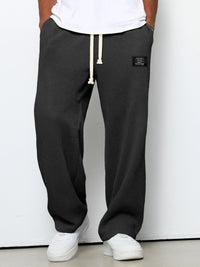 Voorkant van de wafelgebreide broek in donkergrijs, gedragen door een model met wit shirt, wijde pijpen en een crèmekleurig trekkoord. 1