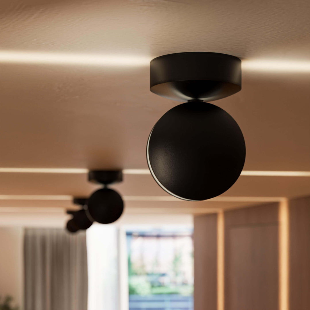 Close-up van een zwarte plafondlamp met ronde kop, met een lichtlijn over het plafond en een tweede lamp wazig op de achtergrond. 11