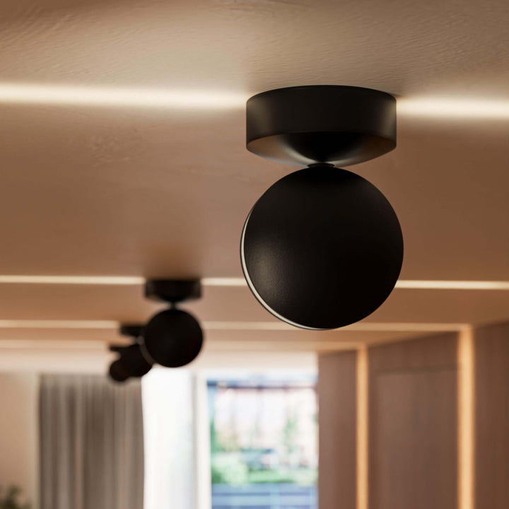 Close-up van een zwarte plafondlamp met ronde kop, met een lichtlijn over het plafond en een tweede lamp wazig op de achtergrond. 11