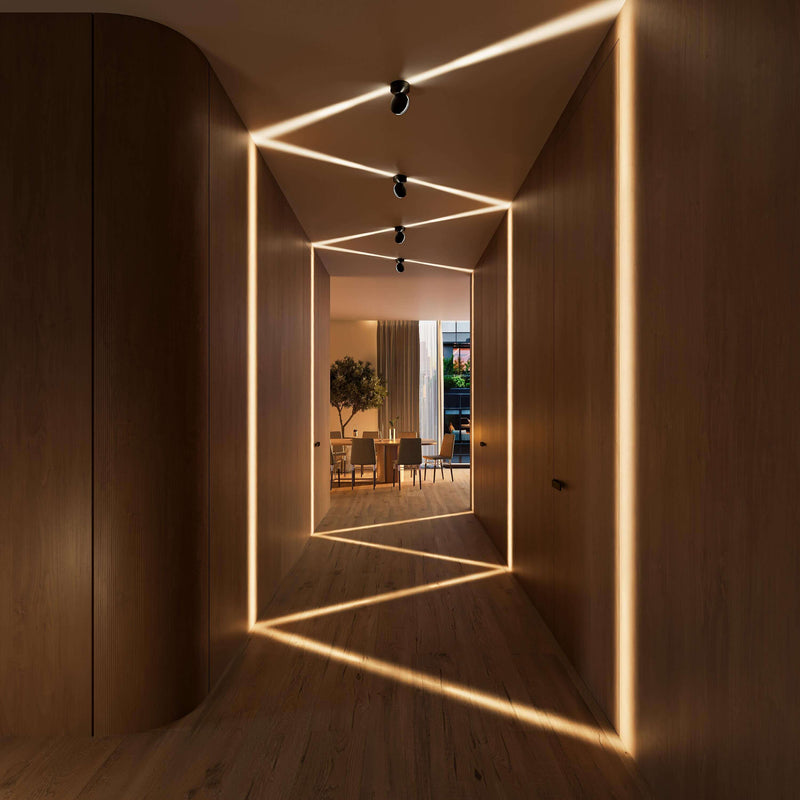 Zwarte plafondlampen in een houten gang werpen zigzaglijnen van warm licht over plafond, wanden en vloer, met een eettafel aan het einde. 10