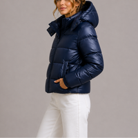Marineblauw glanzend jack met capuchon, zijaanzicht, gedragen door een model met witte broek en hand in zak 1