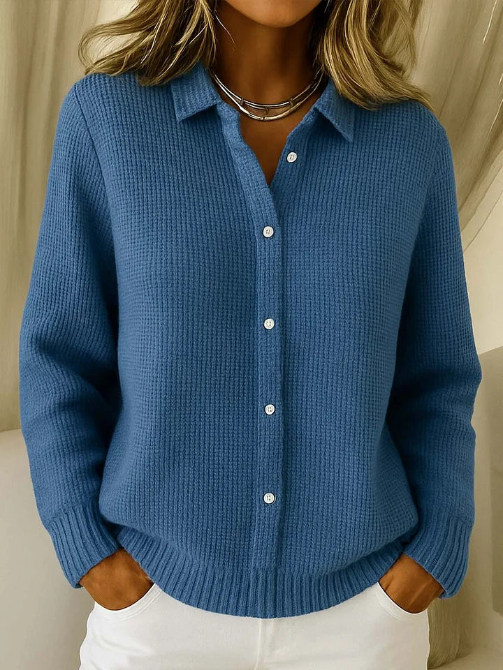De trui in middenblauw, gedragen door een model, met kraag, witte knopen en een zilverkleurige ketting om de hals. 4