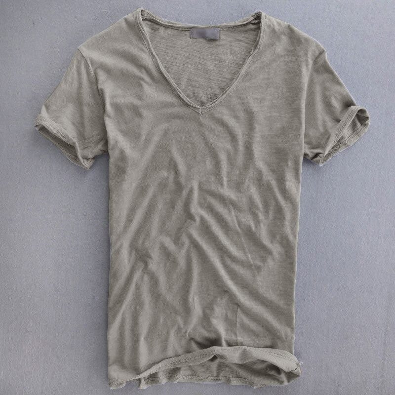 Voorkant van het shirt in grijsbeige op een grijze ondergrond, met diepe V-hals, omgeslagen mouwen en ruwe zoom. 1