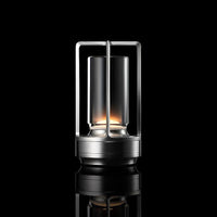 Zilverkleurige lamp met open frame en glazen cilinder, brandend tegen een zwarte achtergrond met spiegeling. 10