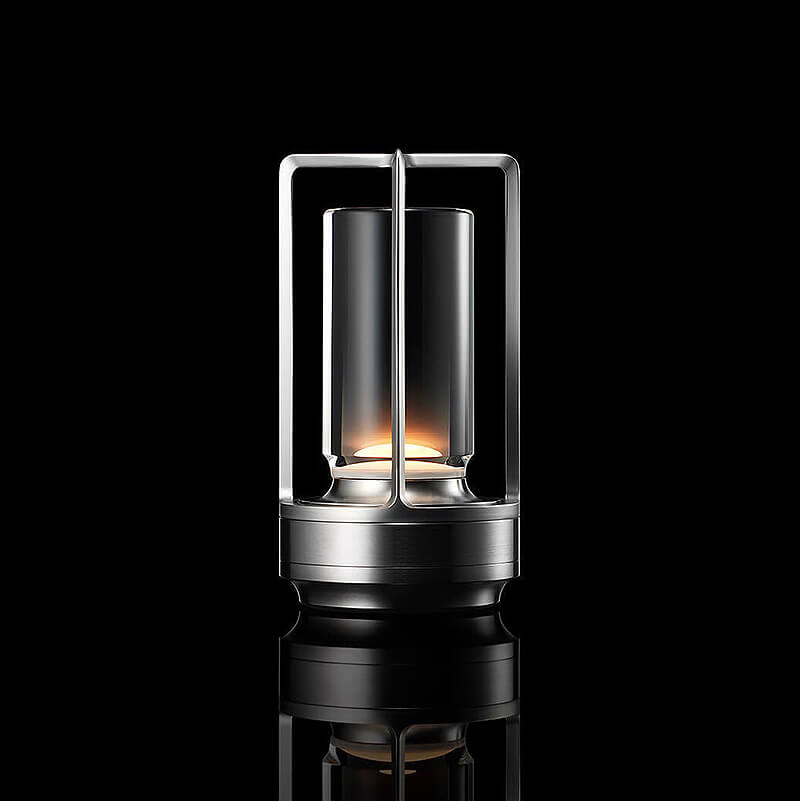 Zilverkleurige lamp met open frame en glazen cilinder, brandend tegen een zwarte achtergrond met spiegeling. 10