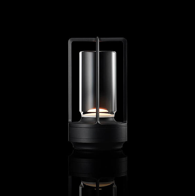 Zwarte lamp met open frame en glazen cilinder, brandend tegen een zwarte achtergrond met spiegeling. 11