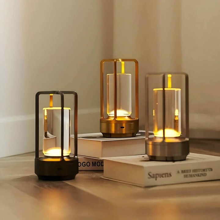 Drie brandende lampen in zwart, goud en zilver naast elkaar op een houten vloer en op boeken. 2