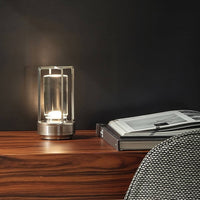 Zilverkleurige lamp brandt op een houten dressoir naast opengeslagen boeken, voor een donkere muur. 5