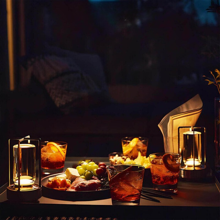 Twee brandende lampen op een tafel met cocktails, een hapjesplank en een servet in de avond. 6