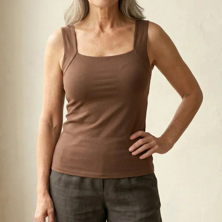 Voorkant van de tanktop in bruin met vierkante hals en brede bandjes, gedragen met een hand op de heup. 2