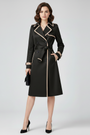 Zwarte uitvoering van de trenchcoat met beige bies, ceintuur in een strik, gedragen door een model met zwarte pumps. 5