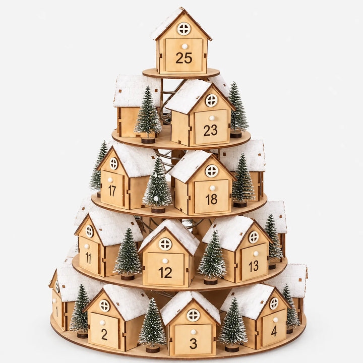 Dezelfde gelaagde adventskalender van houten huisjes met sneeuwdaken en miniatuurdennenboompjes, vrijstaand tegen een witte achtergrond. 2