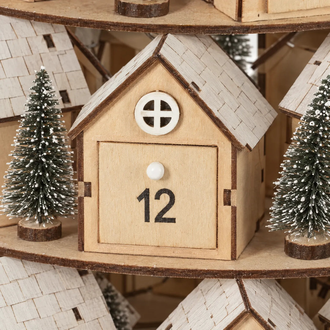Close-up van een houten huisje met rond raampje, wit knopje en dakbedekking van kleine houten plaatjes, tussen twee besneeuwde boompjes. 3