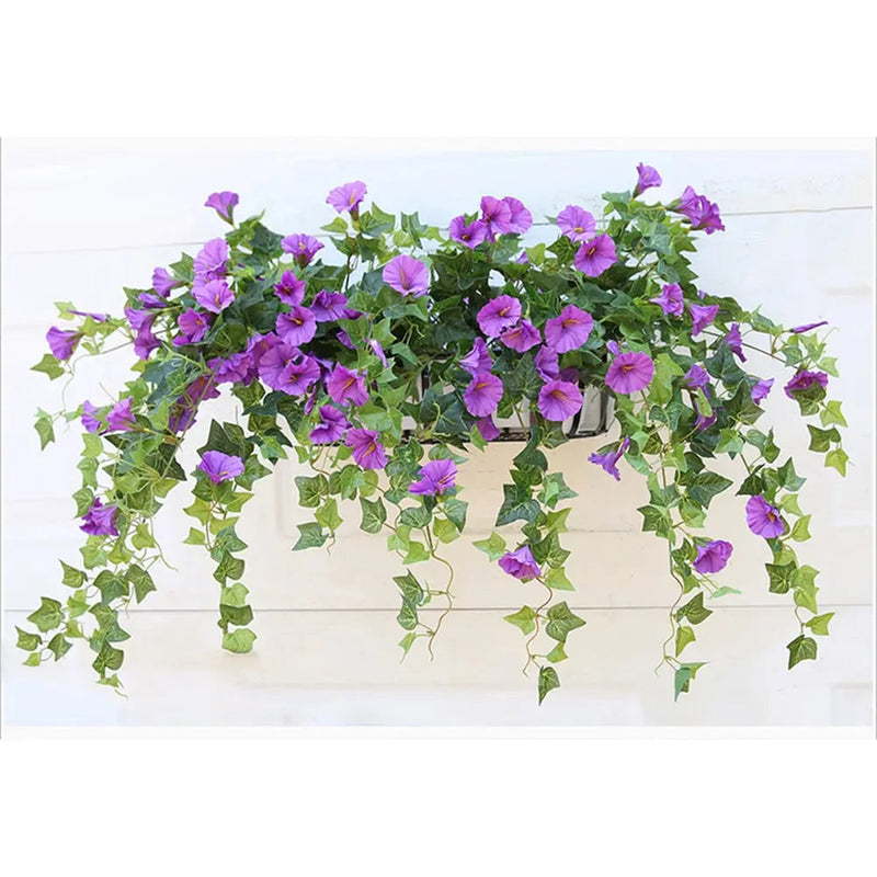 Paarse kunstbloemen met lange hangende groene ranken in een wandbak, opgehangen aan een witte houten muur. 6