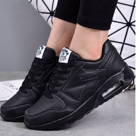 Zwarte sneakers met luchtkussenzool gedragen door een model, met zwarte legging en geometrisch patroon op de achtergrond 2