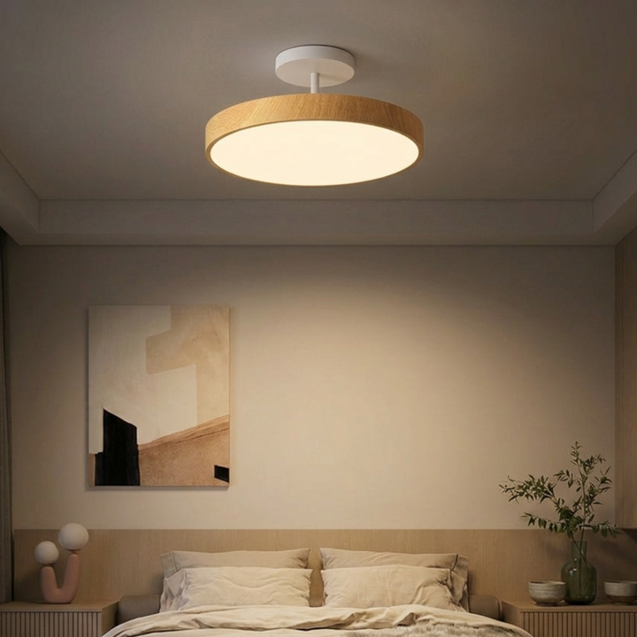 Lichte houtlook plafondlamp met witte steun boven een slaapkamerbed met beige beddengoed en een schilderij aan de muur. 7