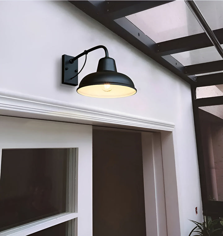 Zwarte wandlamp met lichte binnenkant en brandende lamp boven een deur aan een witte gevel onder een overkapping. 4