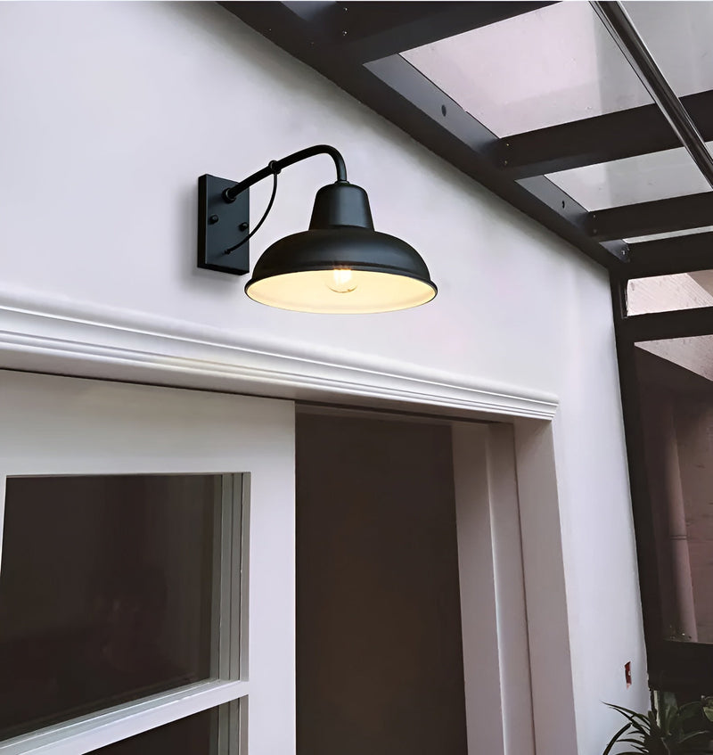 Zwarte wandlamp met lichte binnenkant en brandende lamp boven een deur aan een witte gevel onder een overkapping. 4