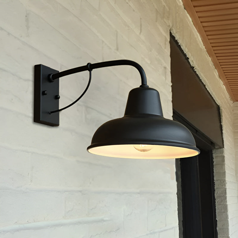 Zwarte wandlamp met brandende gloeilamp tegen een witgeschilderde bakstenen muur naast een zwart kozijn. 5