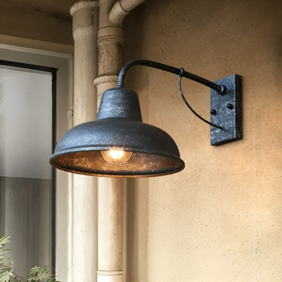 Wandlamp met gespikkelde donkere afwerking en brandende lamp tegen een beige muur naast een regenpijp en venster. 6